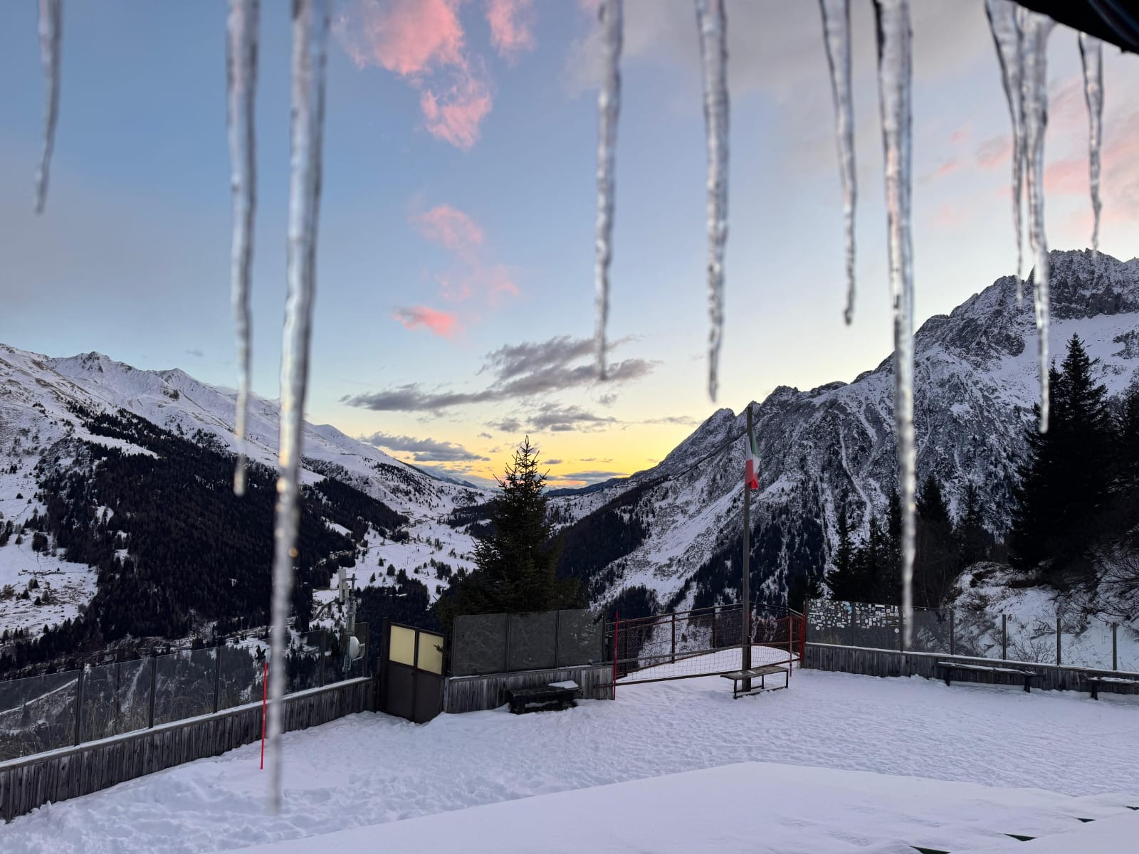 Locandina weekend a Ponte di Legno, con una foto presa da un rifugio, con delle piccole stalattiti di ghiaccio in primo piano e sullo sfondo le montagne e l'alba.
